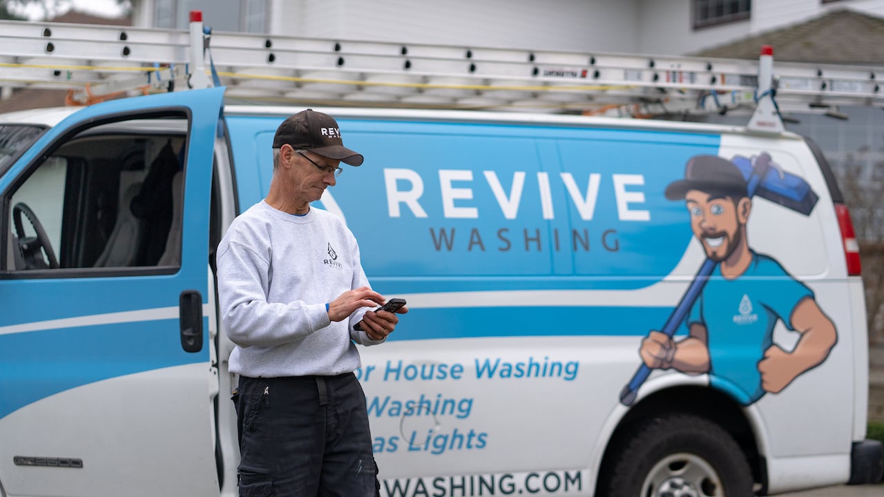 window cleaner standing by work van holding phone