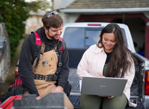 image of two service providers looking at laptop while sitting on flatbed of their truck