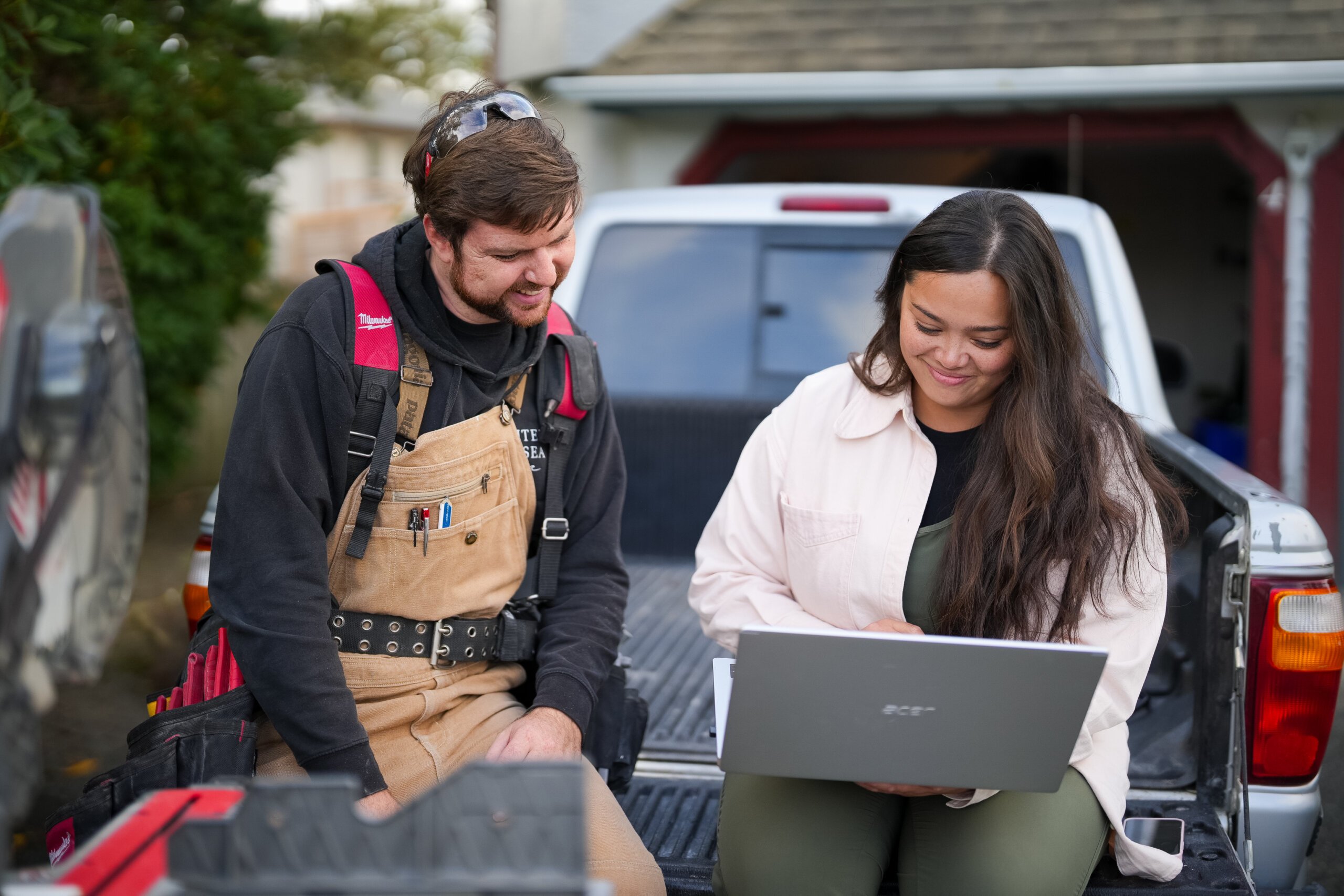 image of two service providers looking at laptop while sitting on flatbed of their truck