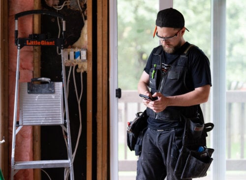 construction worker standing in unfinished room, looking at phone