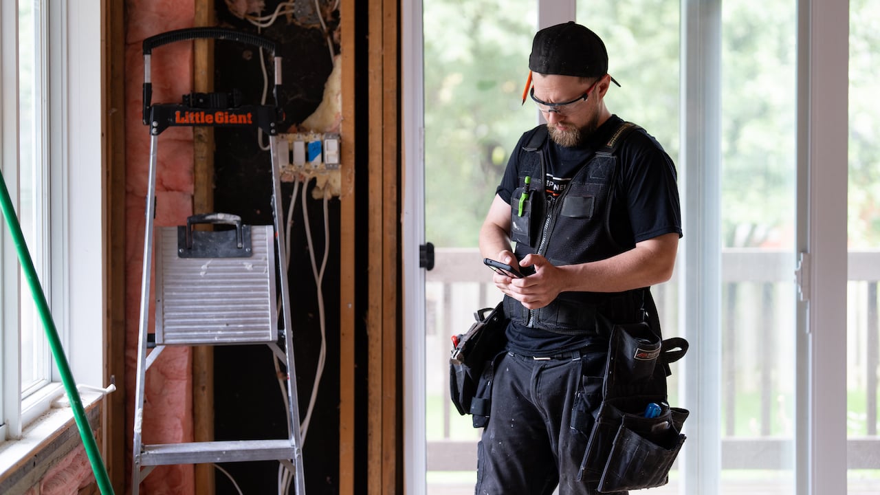 construction worker standing in unfinished room, looking at phone