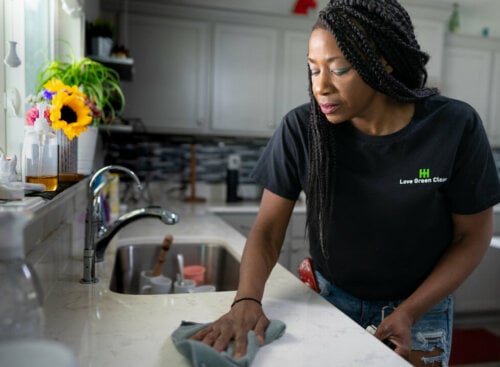 woman cleaning kitchen while wearing shirt with cleaning company name