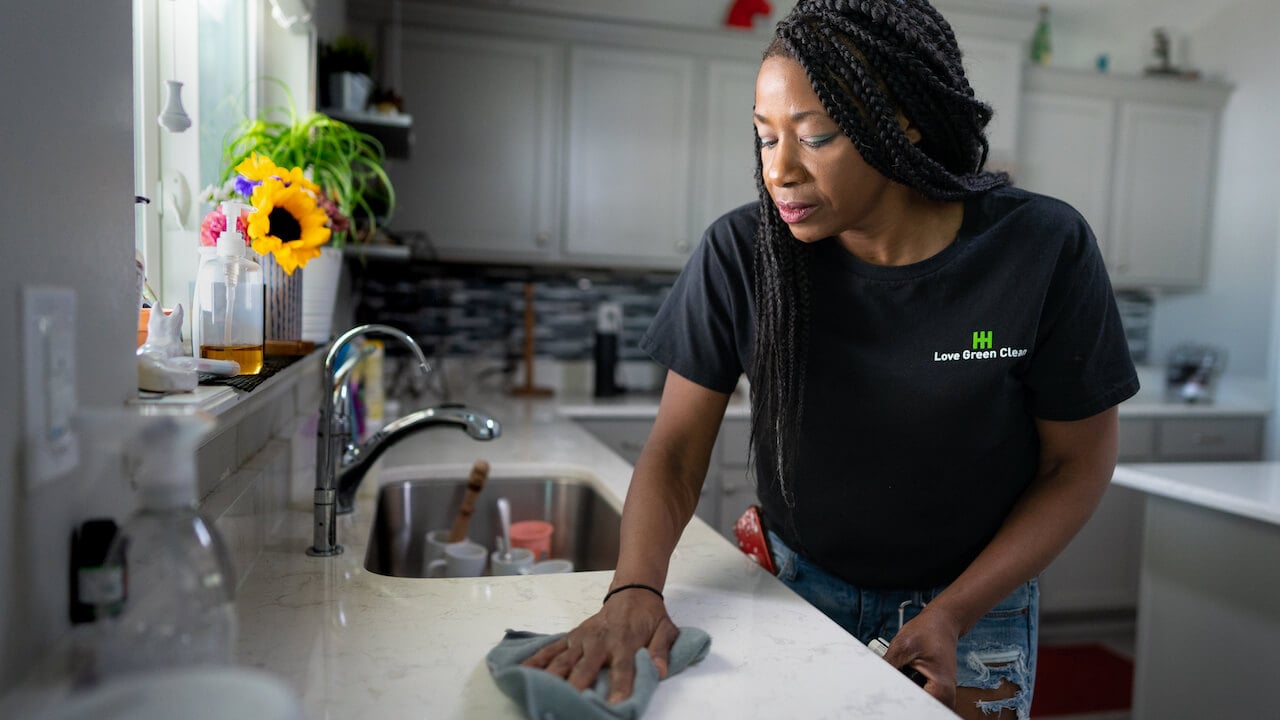 woman cleaning kitchen while wearing shirt with cleaning company name