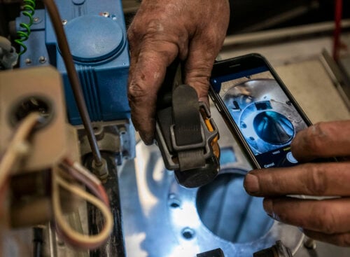 plumber's hands holding a phone and looking into equipment