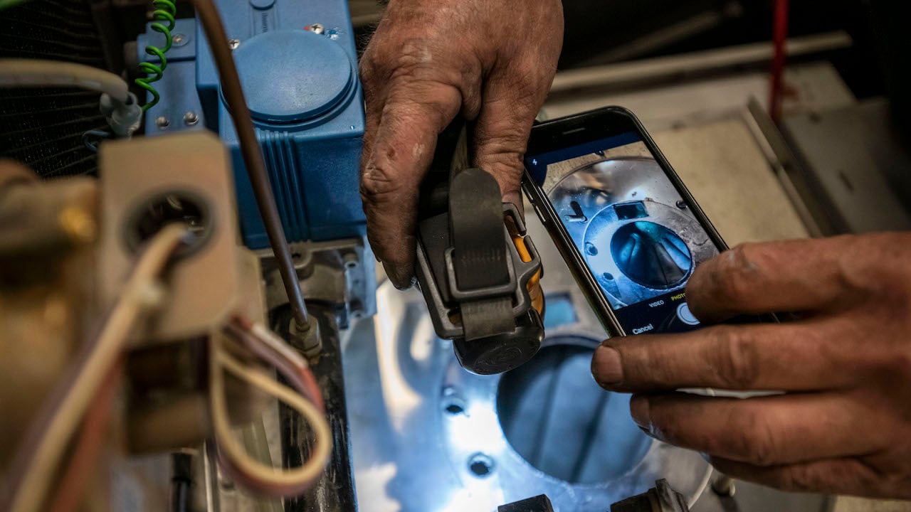 plumber's hands holding a phone and looking into equipment