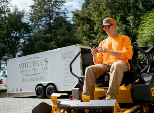 Photo of a lawn care business owner sending an estimate to a customer while sitting on a riding lawn mower outside