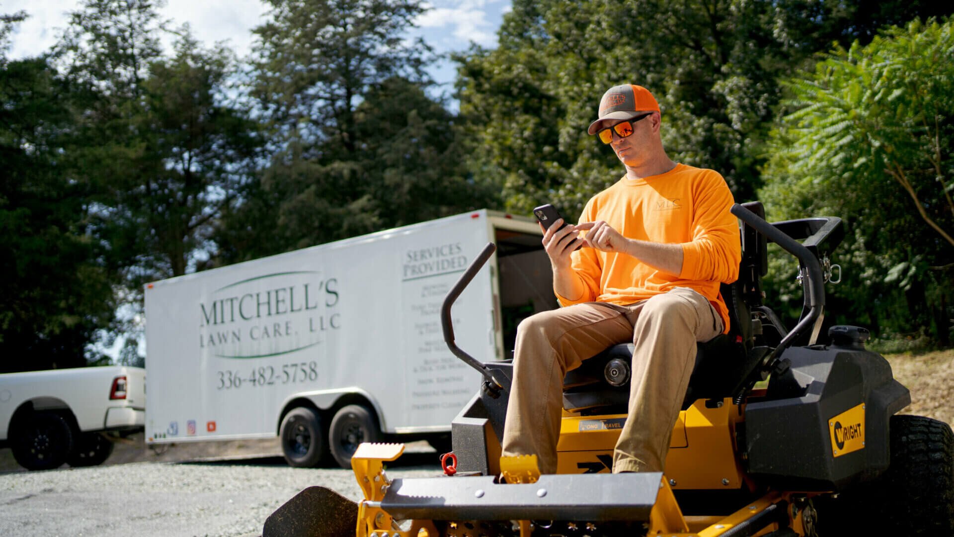 Photo of a lawn care business owner sending an estimate to a customer while sitting on a riding lawn mower outside