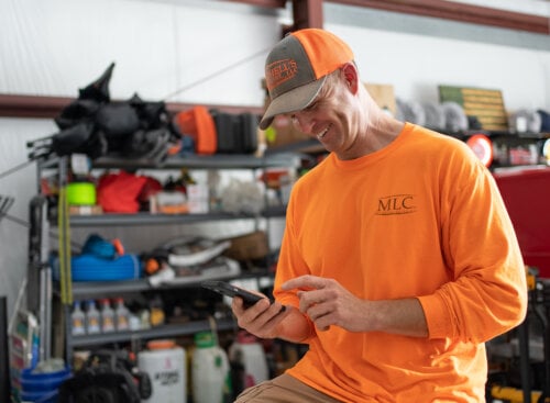 Photo of a lawn care contractor smiling at his phone and using lawn care business apps