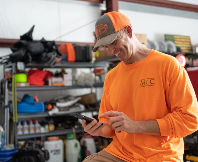 Photo of a lawn care contractor smiling at his phone and using lawn care business apps