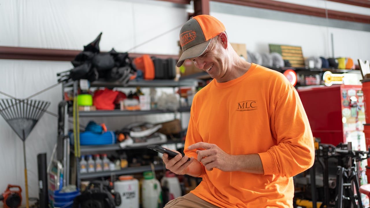 Photo of a lawn care contractor smiling at his phone and using lawn care business apps