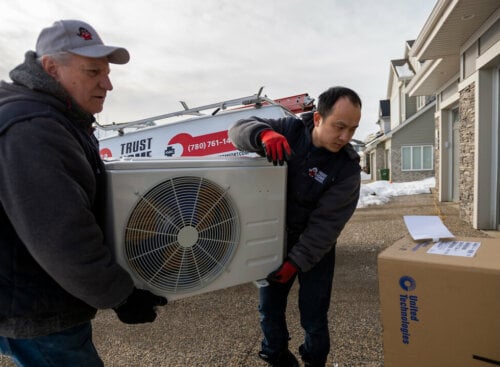 Photo of two HVAC technicians carrying an air conditioning unit to a customer's house