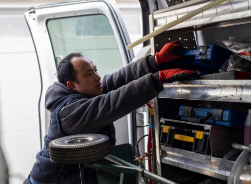 Photo of an HVAC contractor reaching for tools in the back of a service van