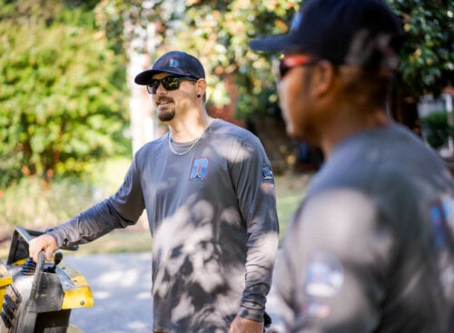 A landscaping business owner and lawn care employee discussing a job outside