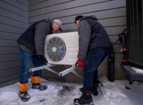 Photo of two HVAC contractor installing an outdoor air conditioning unit outside a house