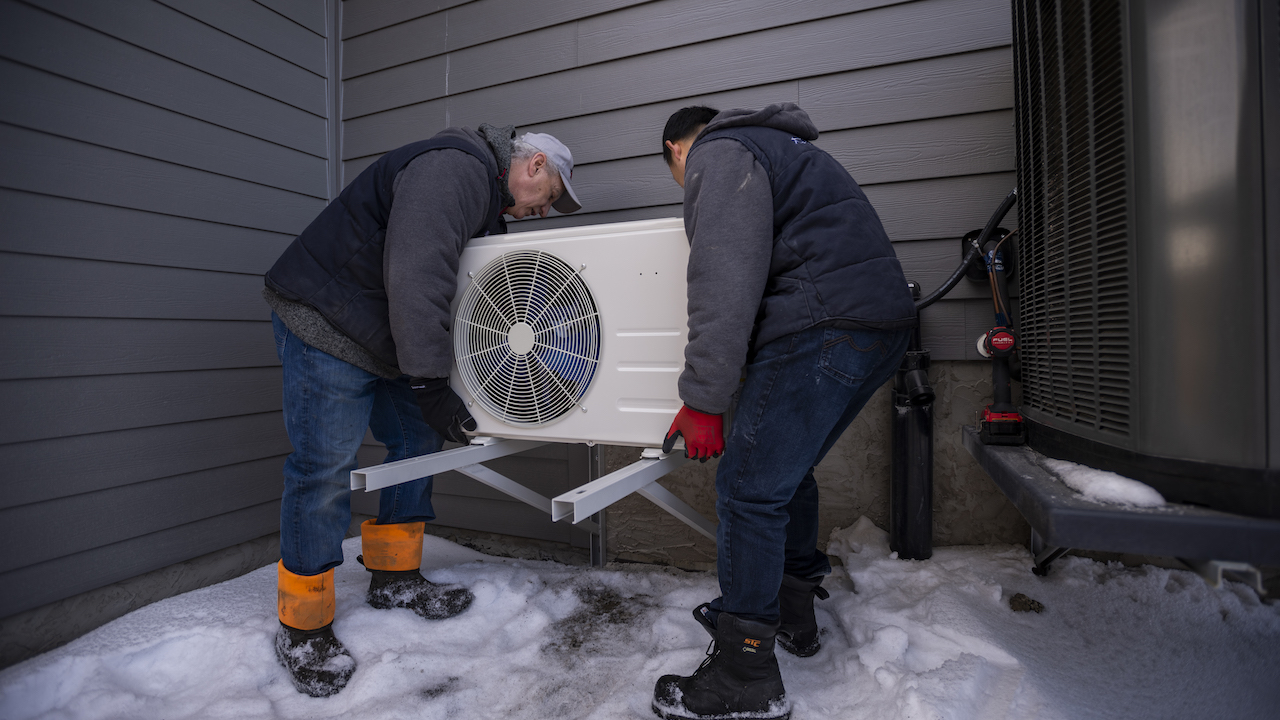 Photo of two HVAC contractor installing an outdoor air conditioning unit outside a house