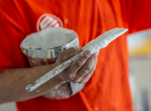 Photo of a painting contractor in an orange Painters Enterprise t-shirt holding a paint bucket and brush