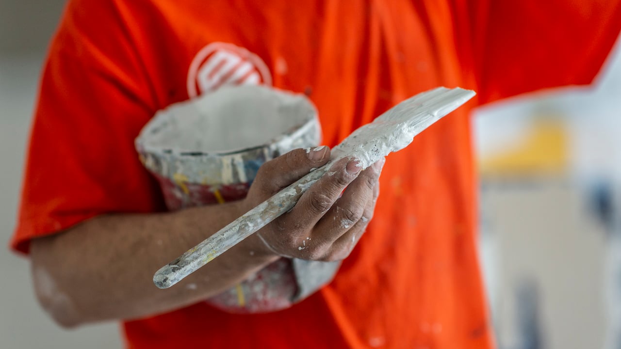 Photo of a painting contractor in an orange Painters Enterprise t-shirt holding a paint bucket and brush