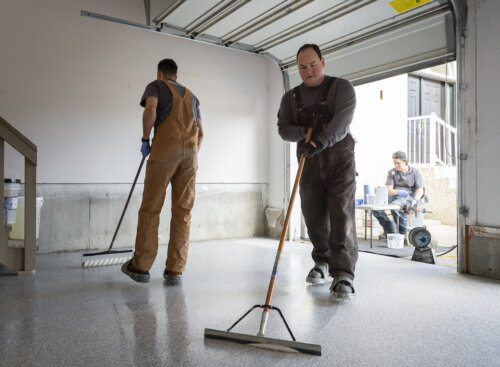 Photo of two painting subcontractors using rollers to buff the floor of a garage