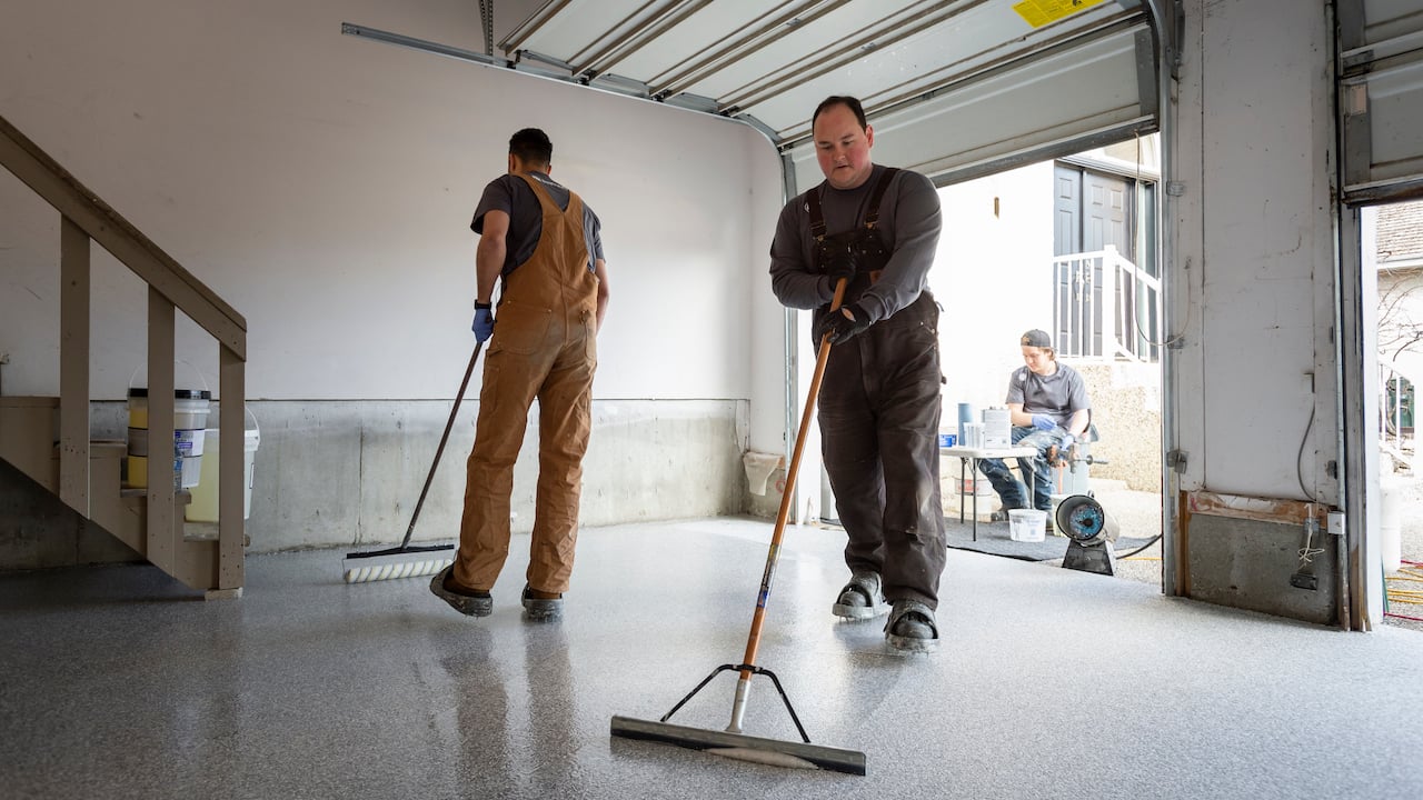Photo of two painting subcontractors using rollers to buff the floor of a garage