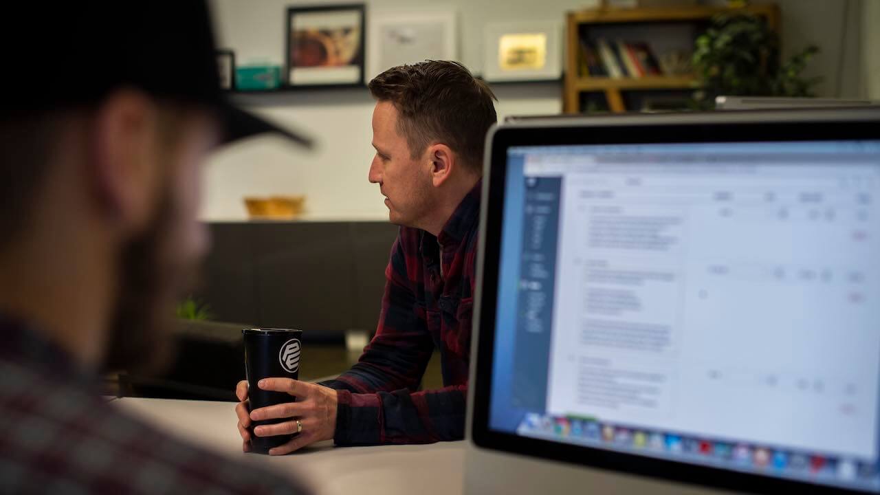 Photo of a painting business owner sitting at a table and a contractor looking at a customer invoice on a computer