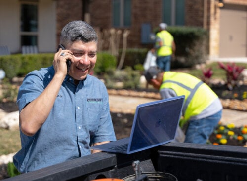 Photo of a landscaping business owner at a client's property phoning a lead from his landscaping website