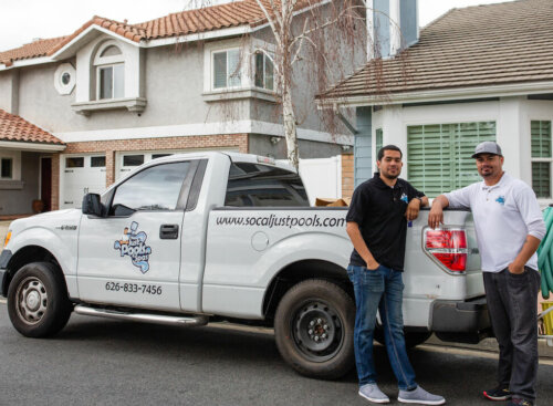 Photo of two lawn care contractors leaning against a company truck outside a client's house