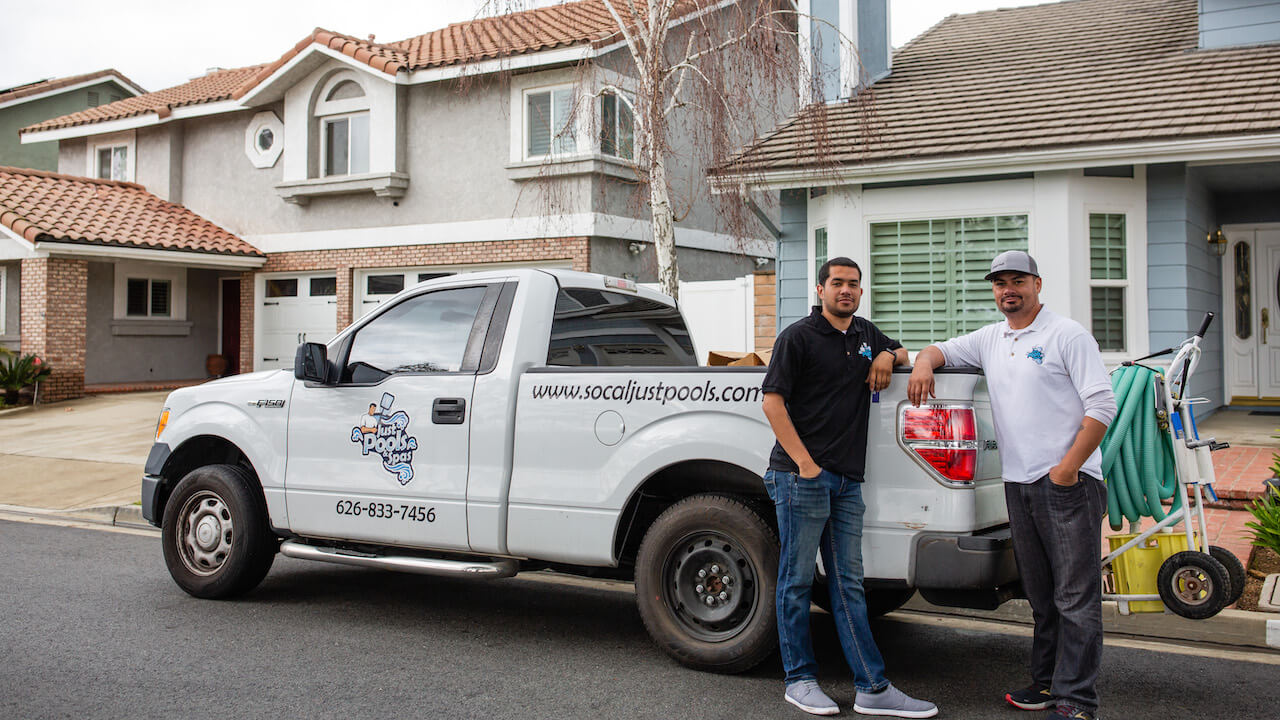 Photo of two lawn care contractors leaning against a company truck outside a client's house