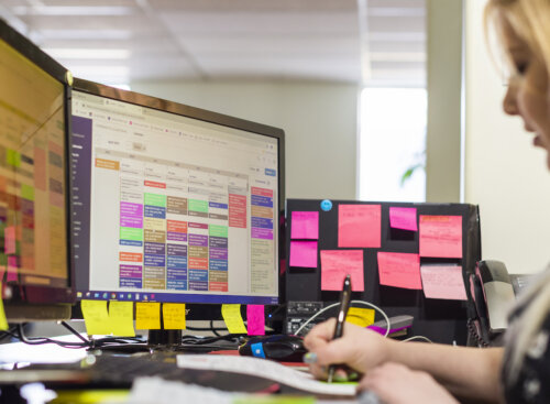 woman working at a desk with computer monitors and sticky notes
