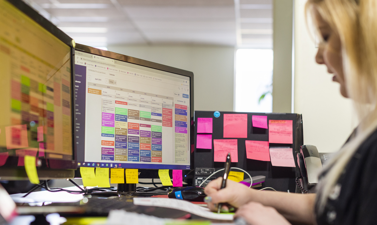 woman working at a desk with computer monitors and sticky notes