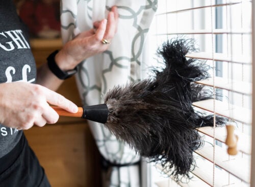 woman feather dusting window blinds