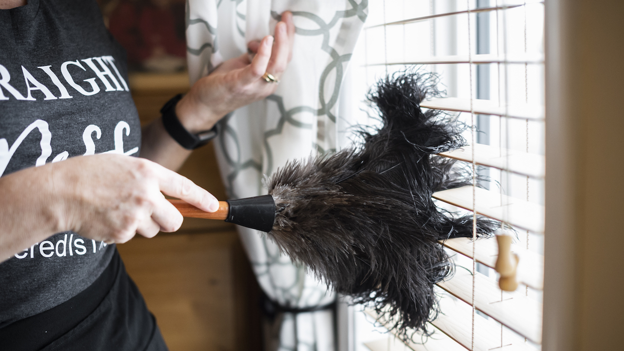 woman feather dusting window blinds
