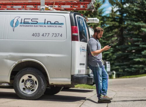 man standing near electrical truck, looking at phone