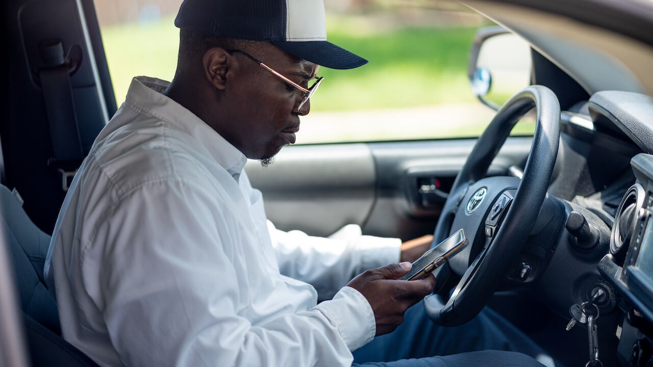 man sitting in car looking at phone in hand