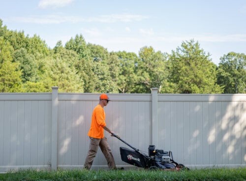 man mowing a lawn in front of a tall white fence