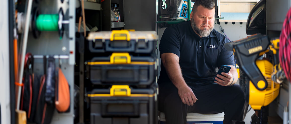 image of electrician sitting in work van looking at his phone