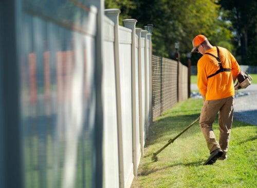 man using weed whacker to trim grass along fence