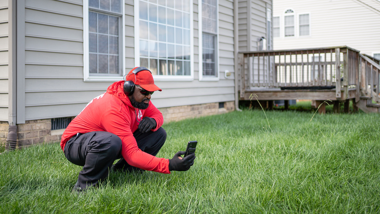 man kneeling down in grass to take photo with phone
