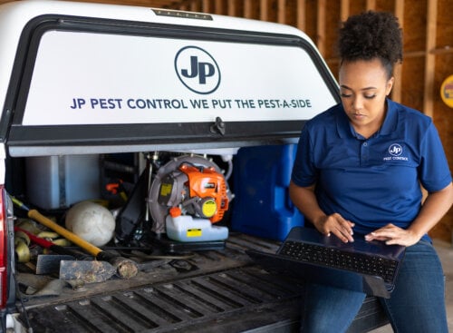 woman sitting in the back of a pest control truck using a laptop