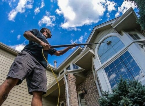 Man cleaning a high window using an extender and brush tool.