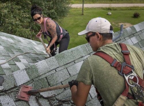 Photo of a roofing contractor and employee removing shingles from a roof