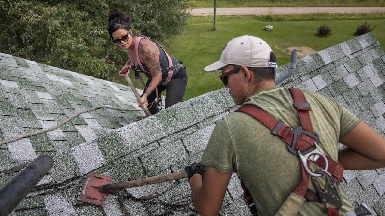 Photo of a roofing contractor and employee removing shingles from a roof