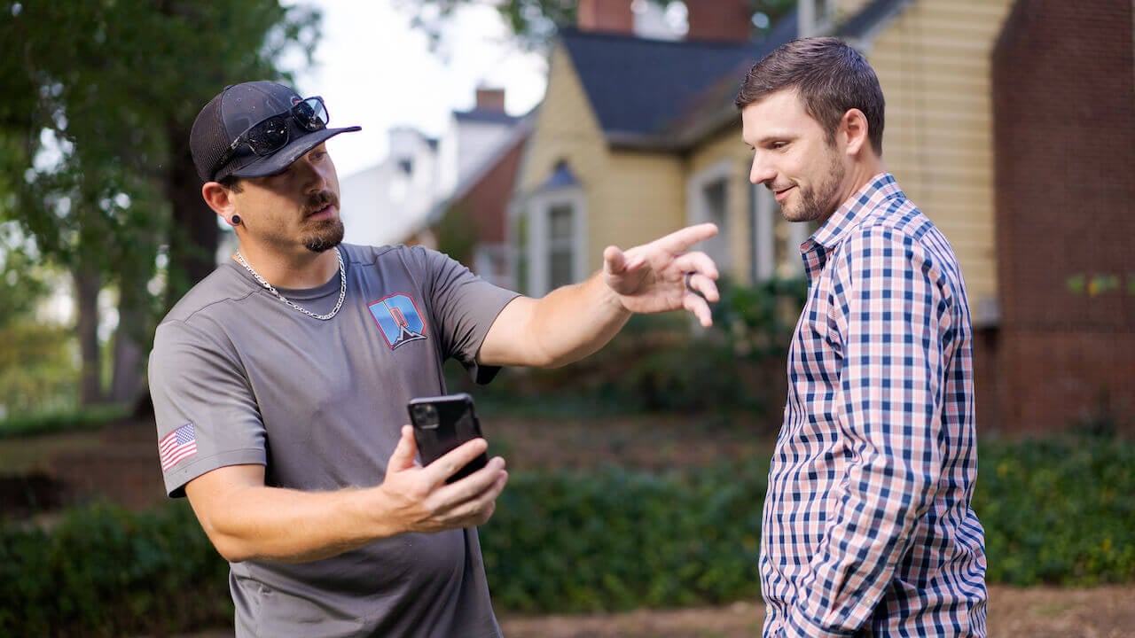 Photo of a home service contractor explaining a job to a client while holding a smartphone