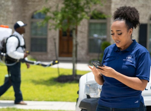 Photo of a small business owner calculating profit margins on her smartphone outside a client's house