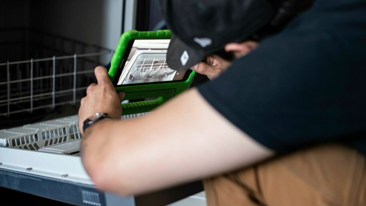 Photo of an appliance repair contractor using an appliance repair app to fix a dishwasher