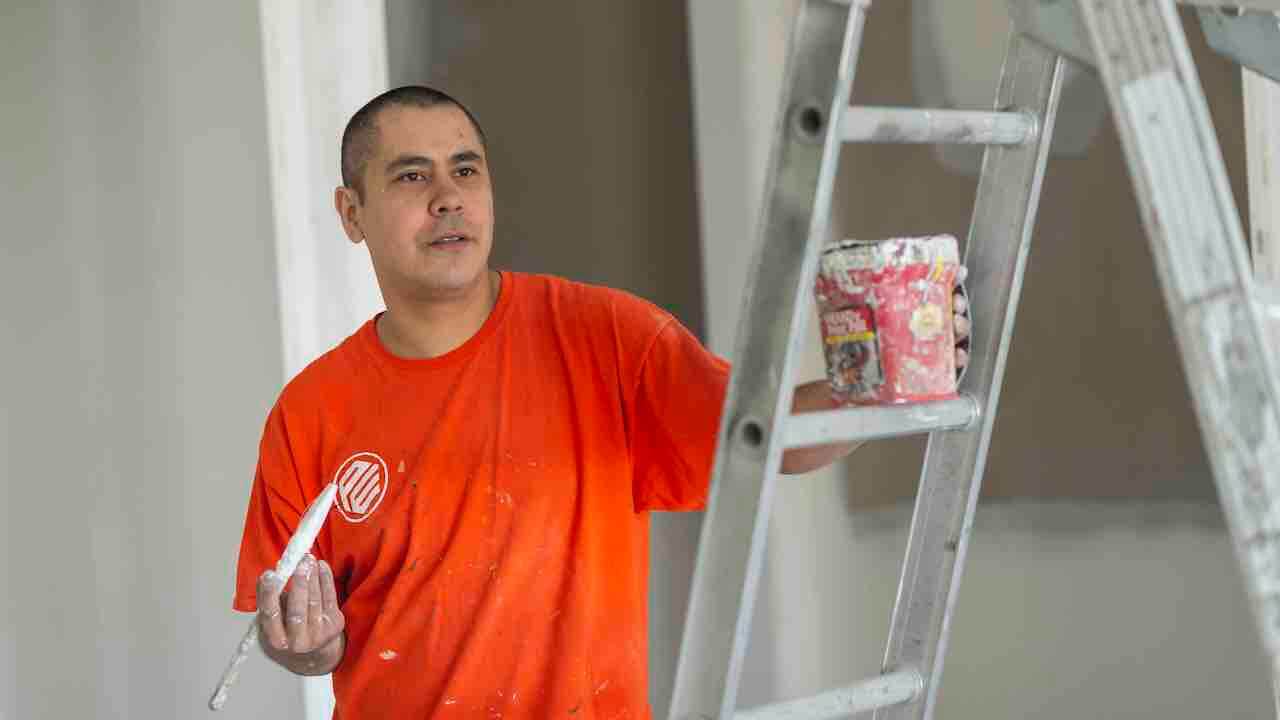 painter holding brush and paint can near ladder