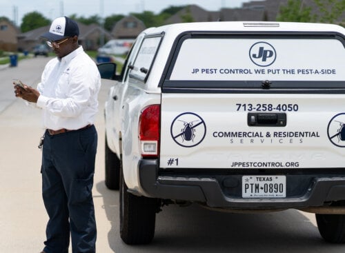 Photo of a pest control business owner standing beside company truck while using pest control apps to manage his business