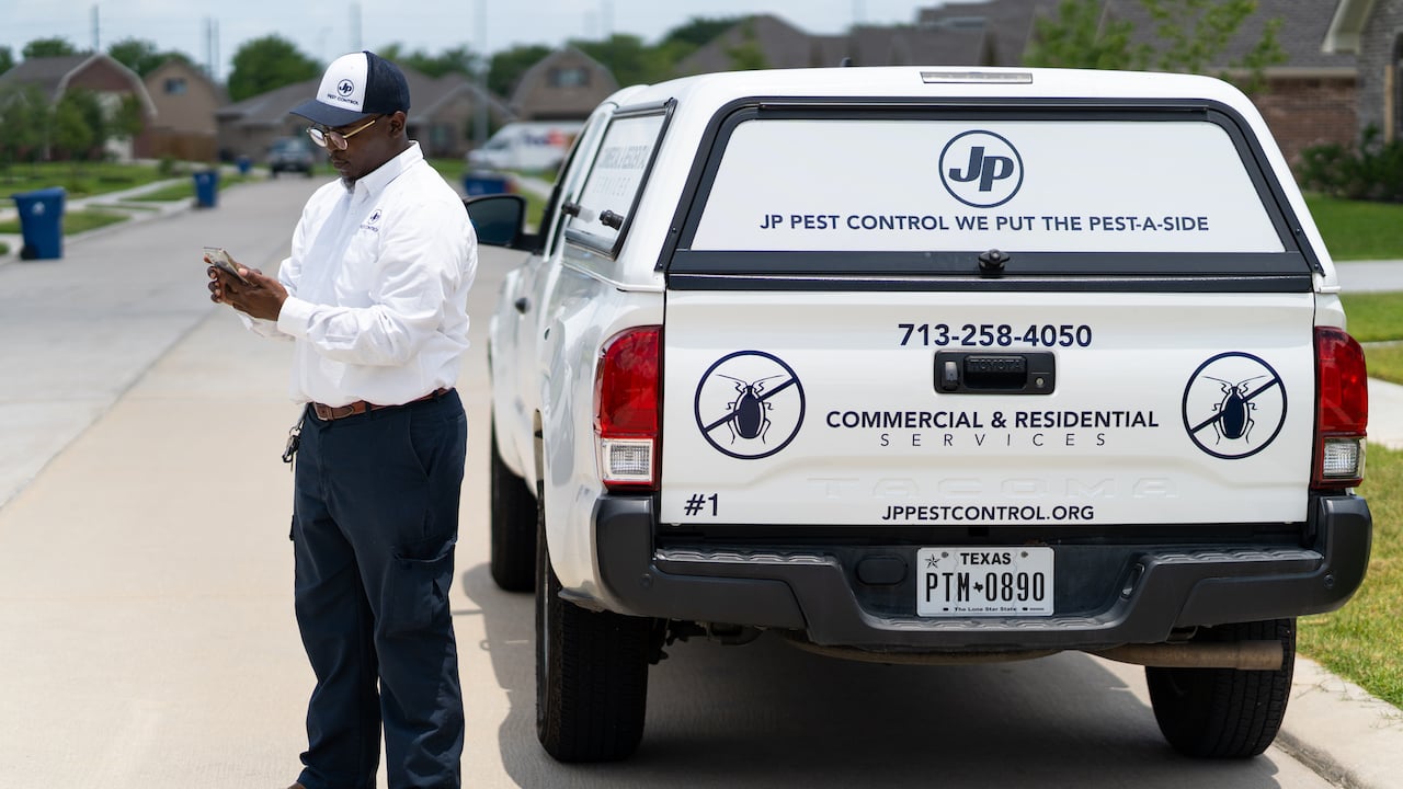 Photo of a pest control business owner standing beside company truck while using pest control apps to manage his business