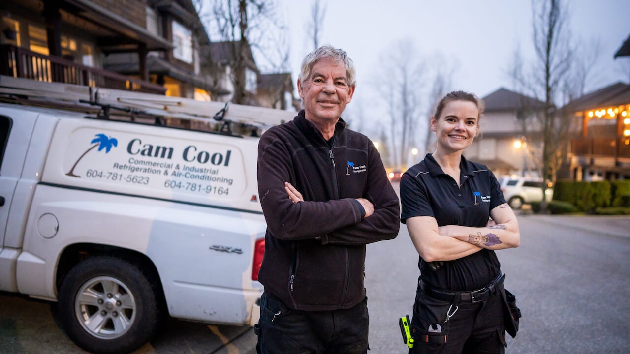 two HVAC professionals standing in front of a work vehicle with the HVAC company name on the side