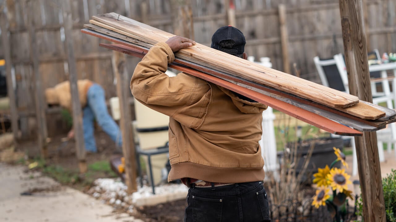 man carrying fence boards