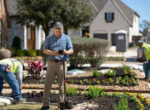 marketing for landscapers - landscaper holding phone and standing on front lawn with workers behind him